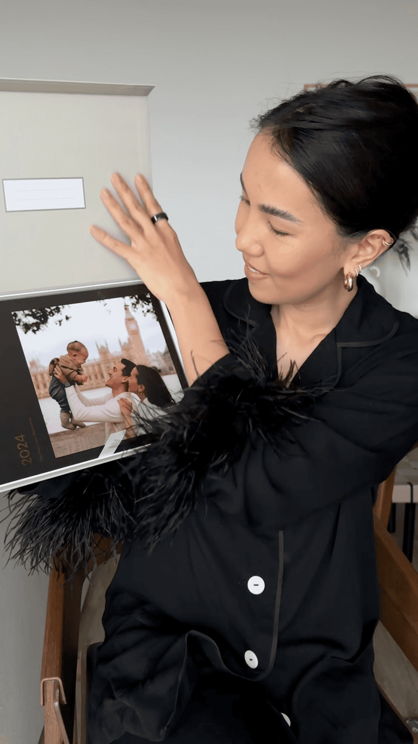 Woman in black outfit showing a photo book in a presentation box with a cover image of a couple and child outdoors.
