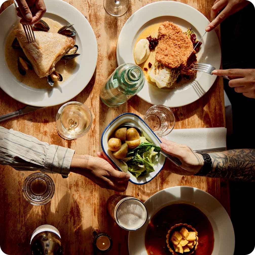 Aerial shot of hands passing food across the table with laden plates in the background.