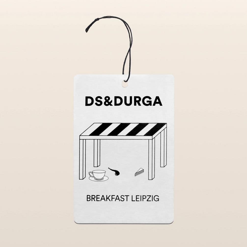 White tag featuring a minimalist table illustration with a cup, spoon, and wedge, and the text "DS & DURGA" and "BREAKFAST LEIPZIG."