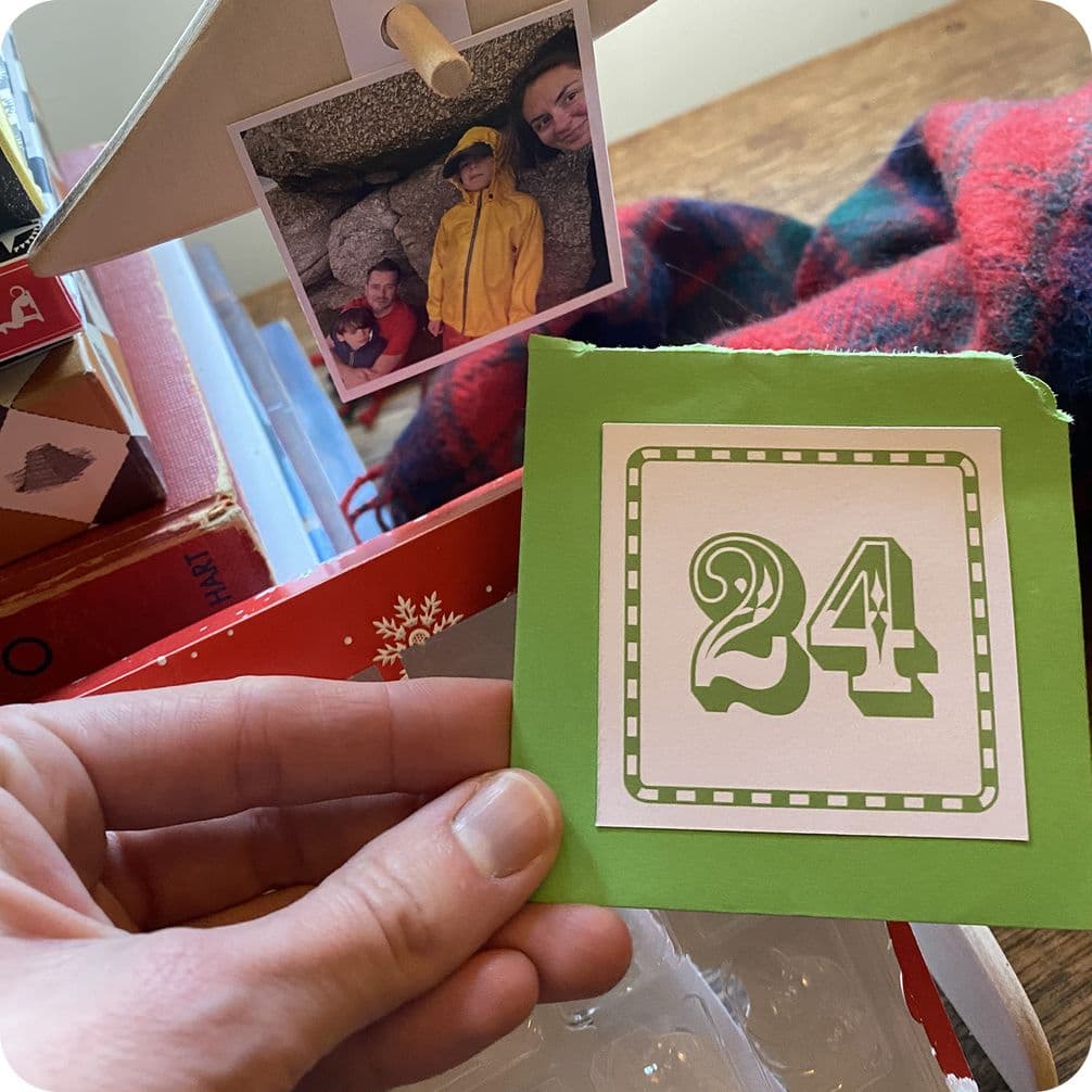 Hand holding a green card with "24" on it, next to a photo of children and a red plaid fabric.