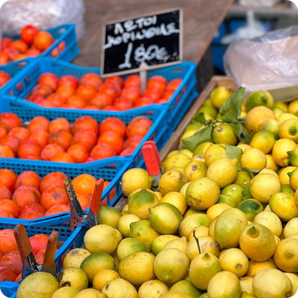 Fresh lemons and tomatoes in blue crates at a market stall, with a price sign in the background.