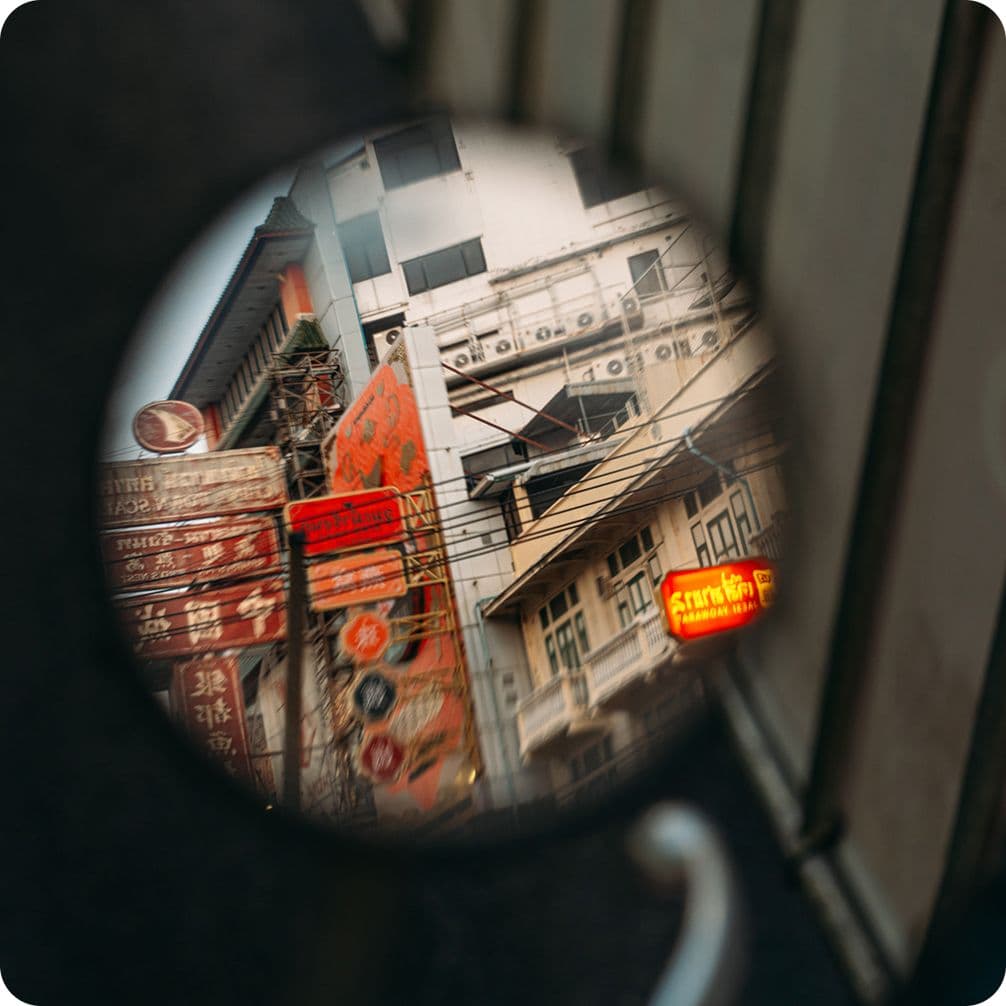 Reflection in a round mirror of a narrow city street with old buildings, red Chinese signs and tangled overhead wires.