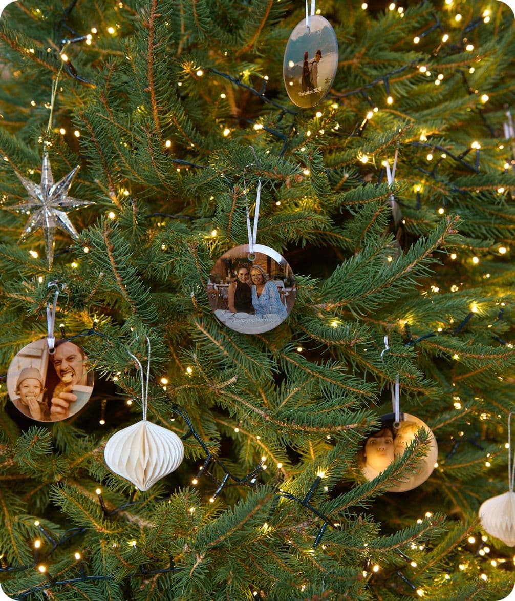 Christmas tree with glowing lights, star ornament, and photo ornaments showing various people, creating a festive and personal holiday display.
