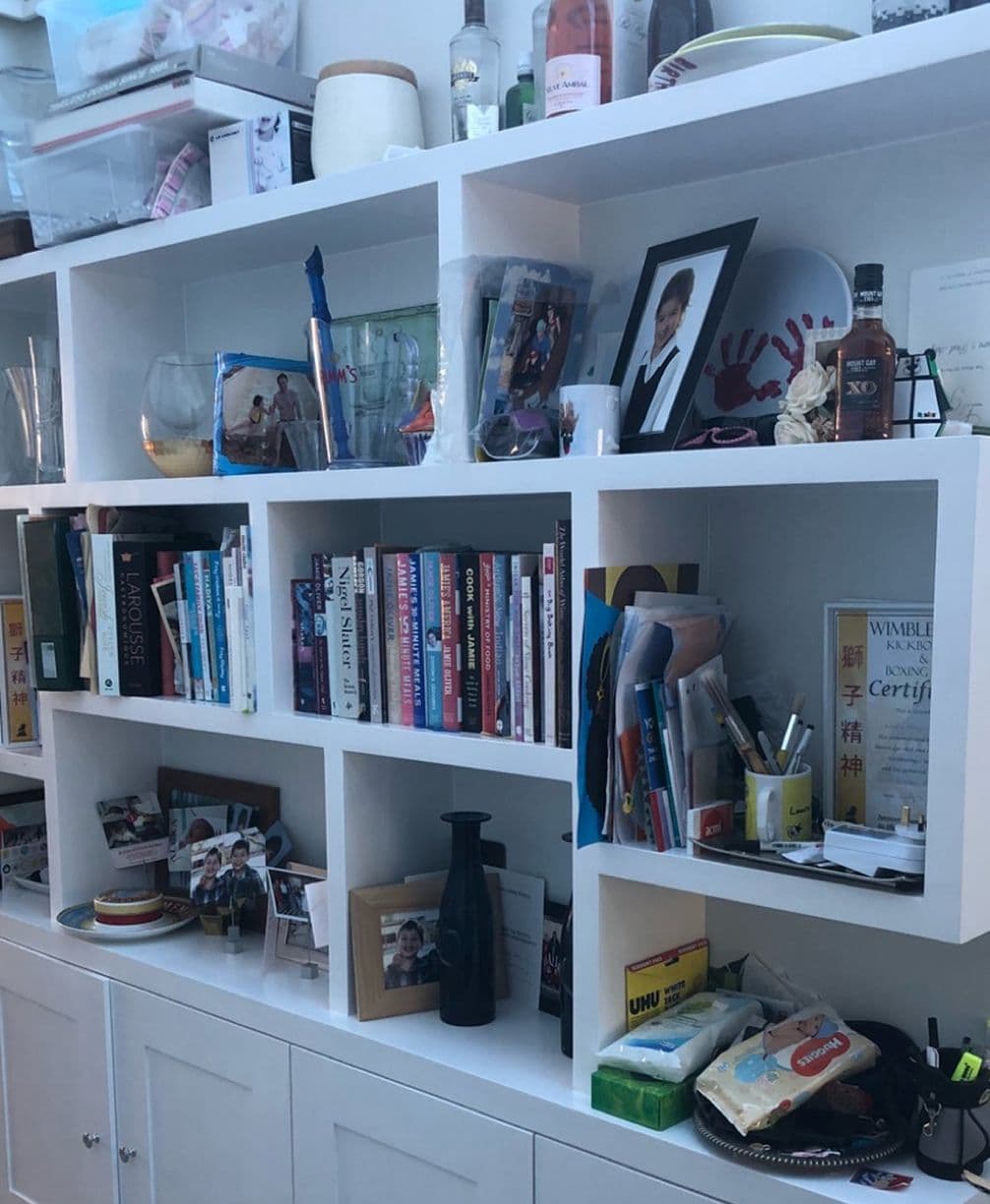 White cubby bookshelf filled with books, framed photos, bottles, stationery, snacks and decorative items.