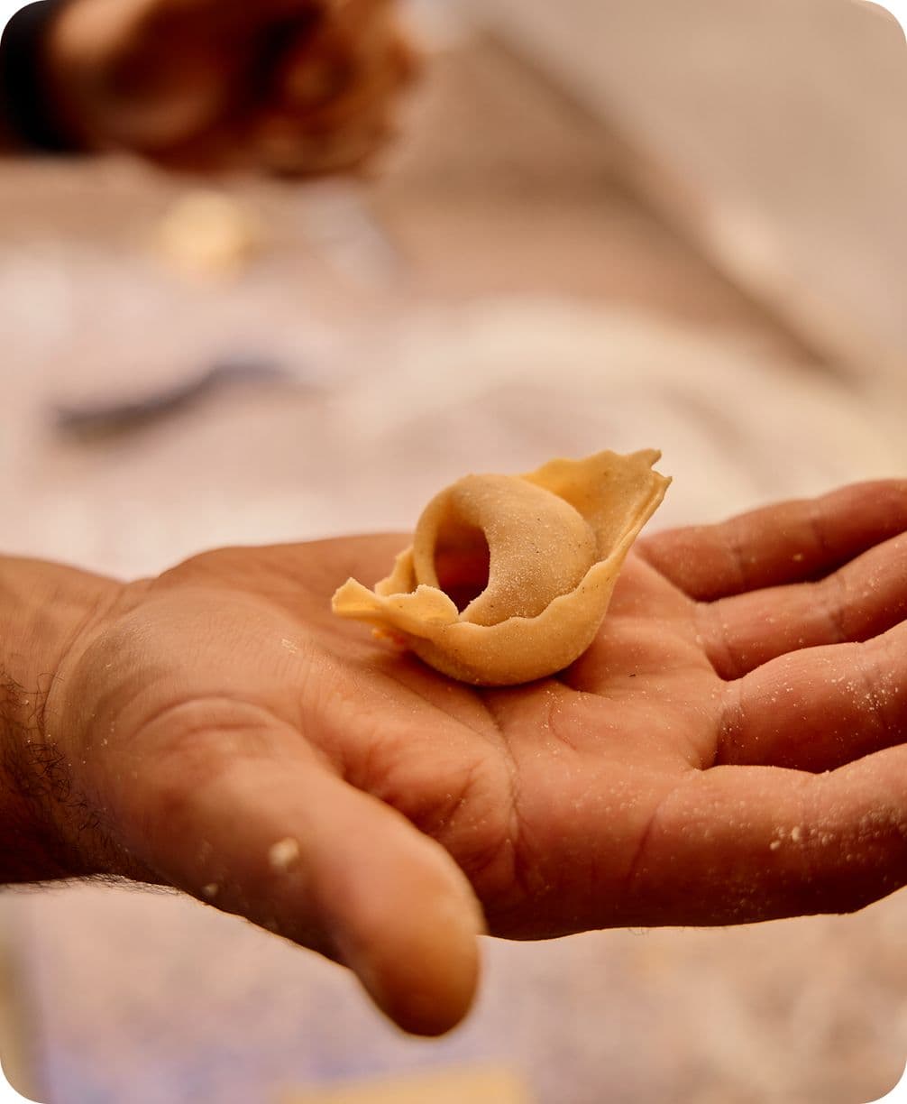 Hand holding a single uncooked tortellini on the palm, flour-dusted skin and soft warm lighting.