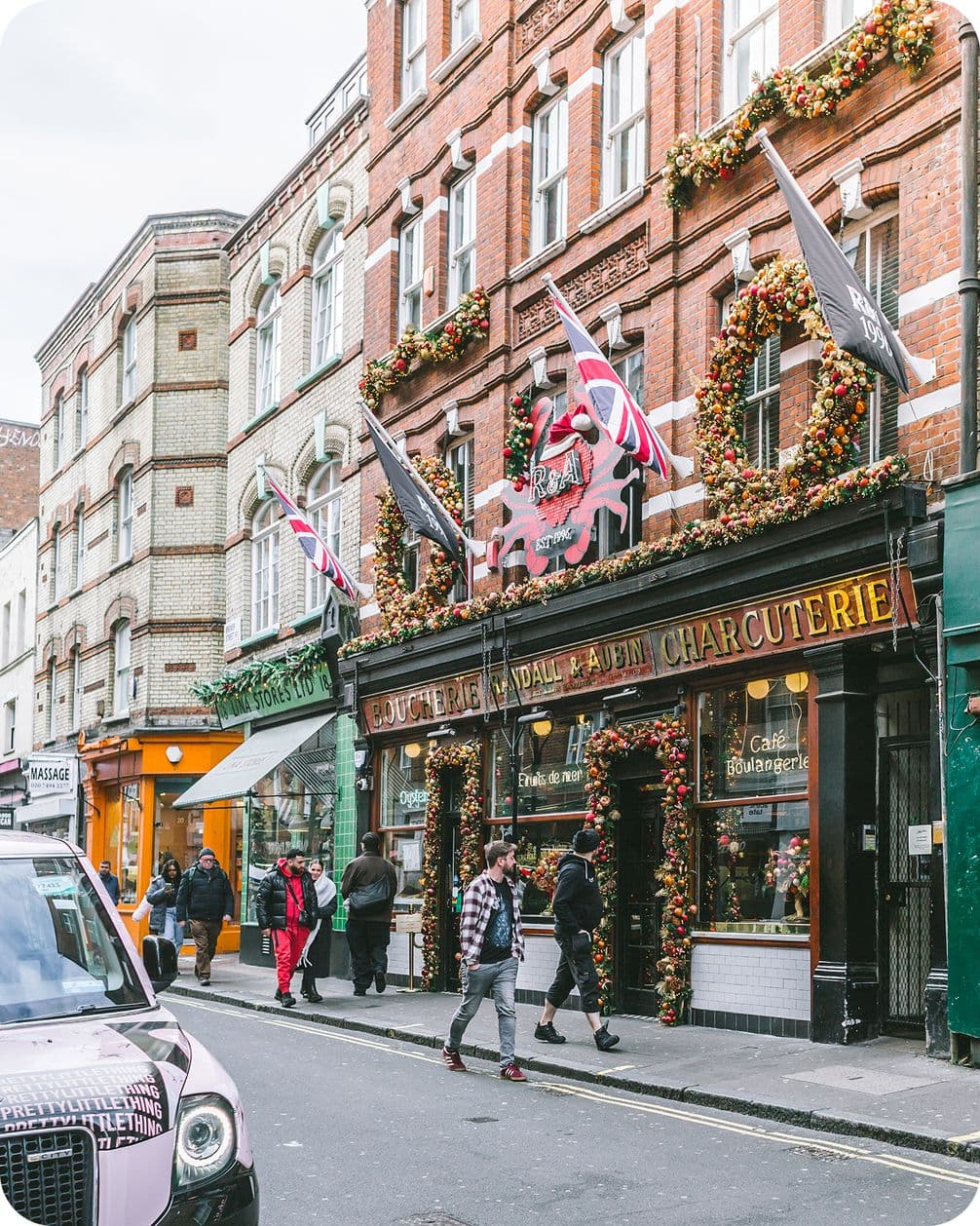 Street view of a charming charcuterie with festive decorations and British flags, surrounded by pedestrians and adjacent shops.