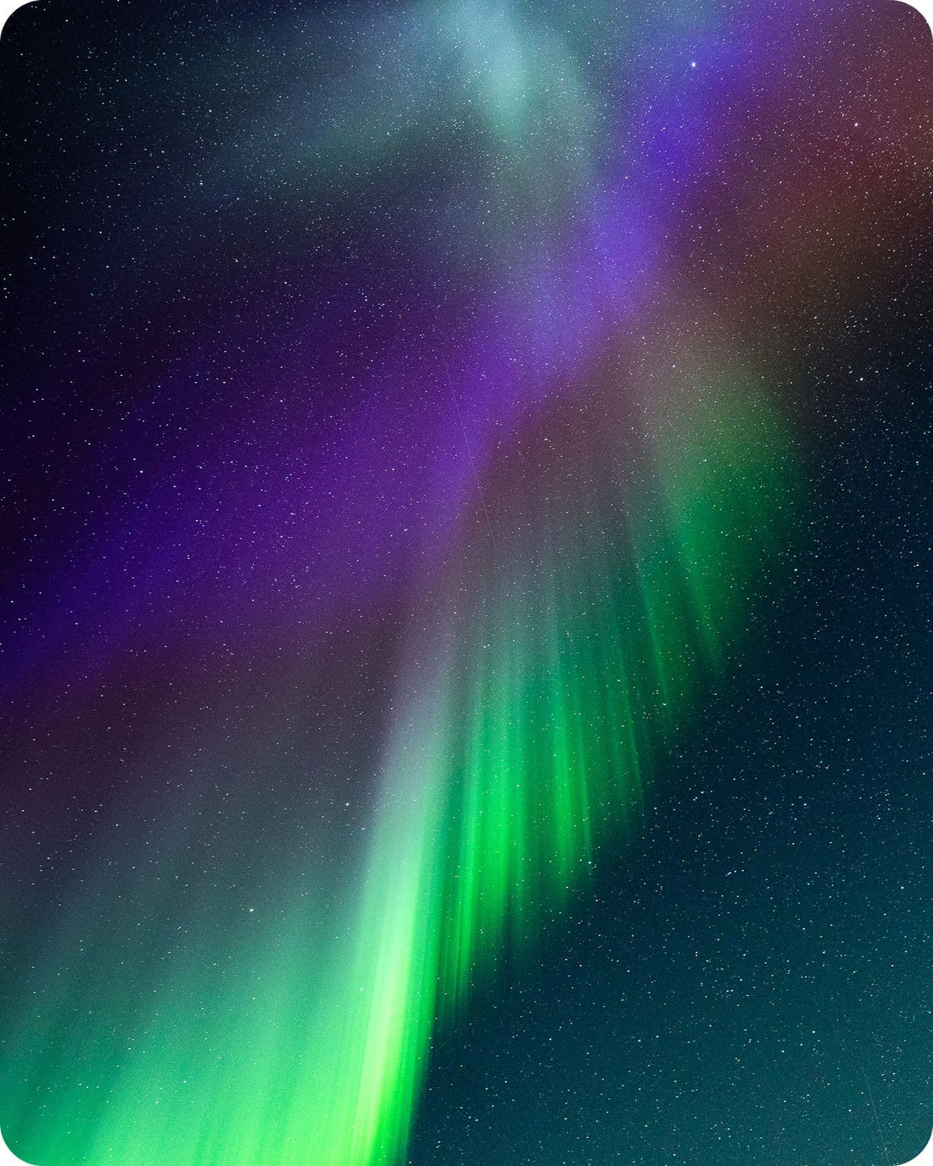 Vibrant aurora borealis with green, purple, and red hues streaking across a starry night sky.