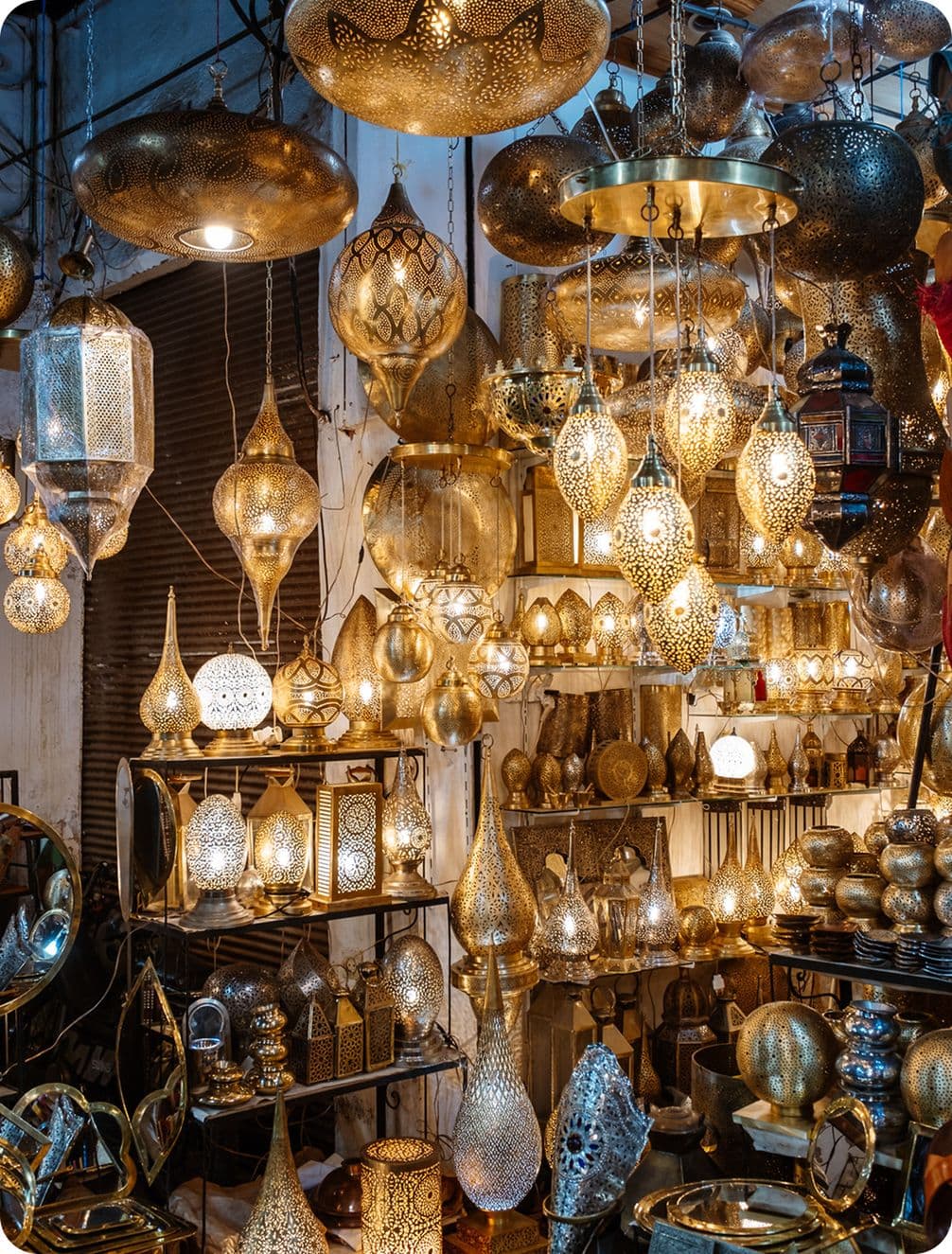 A vibrant display of intricately designed brass lanterns and lamps, emitting a warm glow in a market setting.