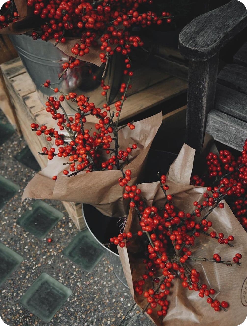 Bouquets of vibrant red berries wrapped in brown paper, displayed in metal buckets on a rustic wooden surface.