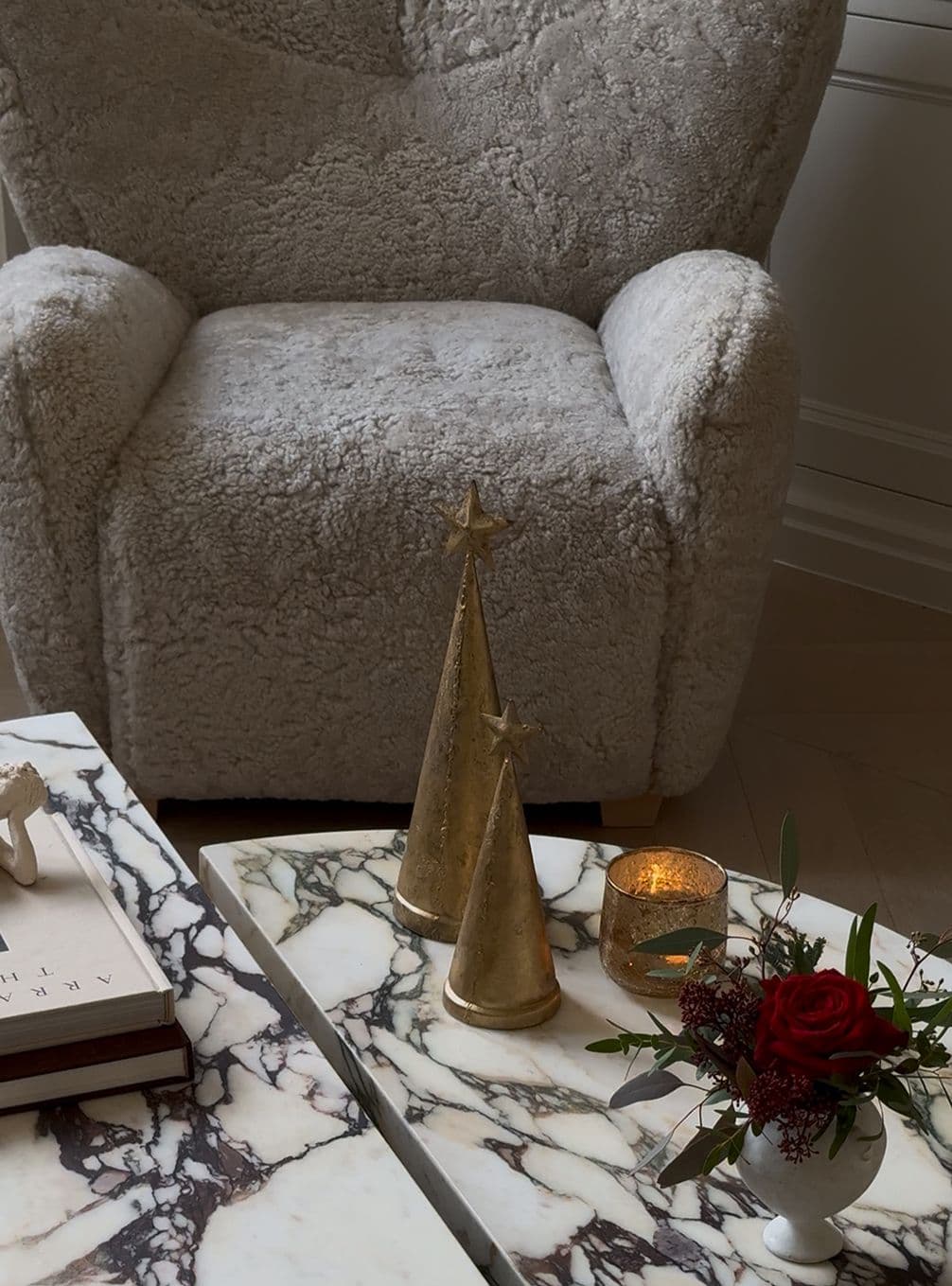 Cozy chair with a marble table featuring gold cone decorations, a lit candle, and a small vase with a red rose and greenery.