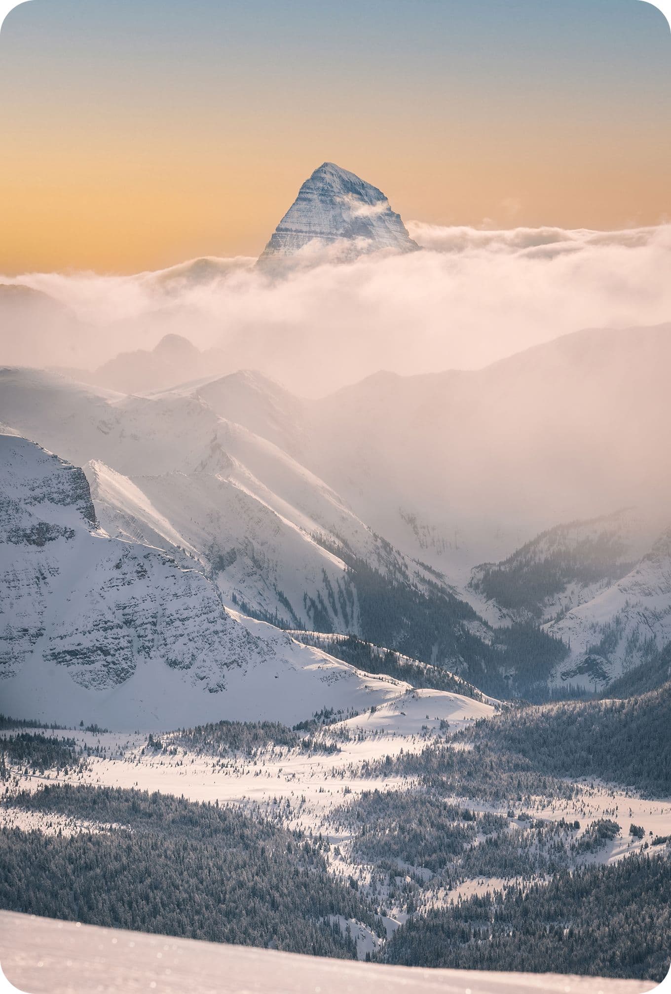Snow-covered mountains with a prominent peak emerging through clouds at sunrise, creating a serene and majestic landscape.