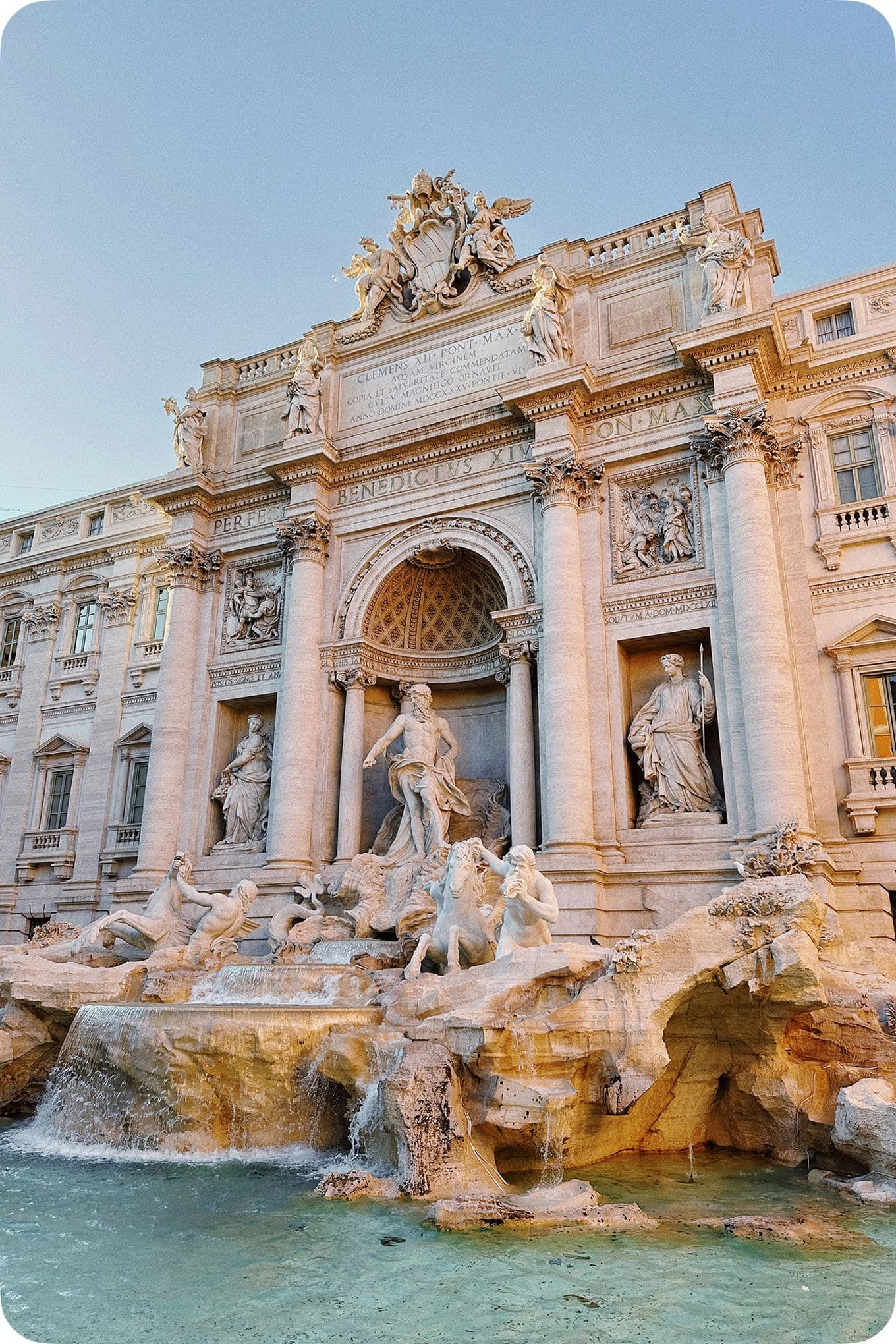 The Trevi Fountain in Rome, Italy, featuring ornate sculptures and cascading water against a clear sky.