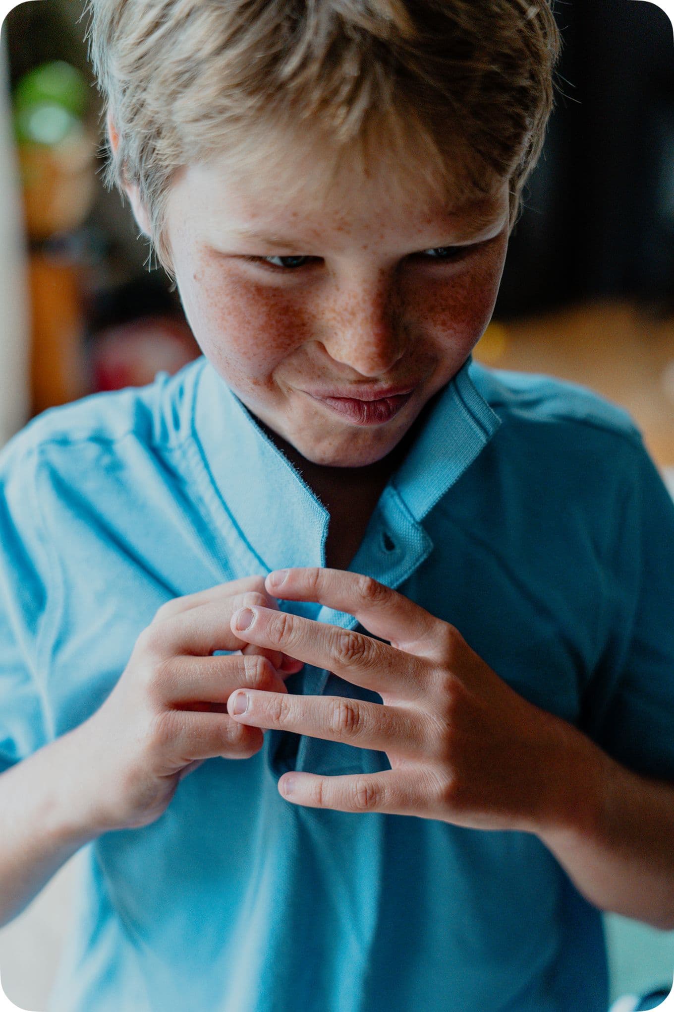 Young boy with freckles and a mischievous smile, adjusting his blue shirt collar with both hands.