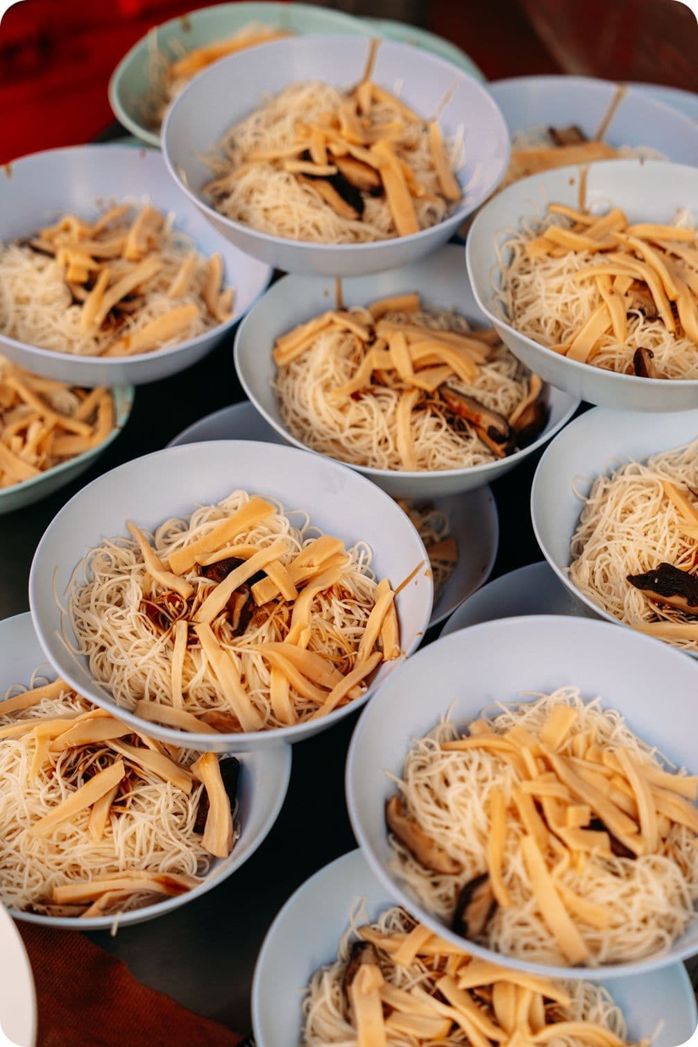 Several light-blue bowls filled with thin rice vermicelli noodles topped with shredded yellow bamboo shoots and dark mushrooms, arranged in a cluster.