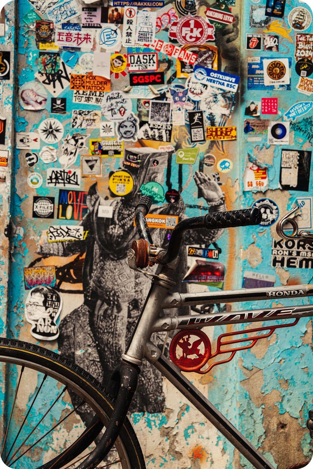 Old bicycle leaning against a peeling blue wall covered in colorful stickers and a black-and-white stencil portrait.
