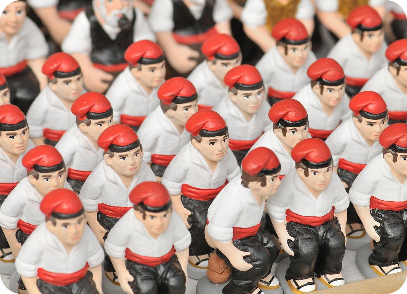 Rows of small figurines wearing white shirts, red berets, and red sashes, standing closely together.