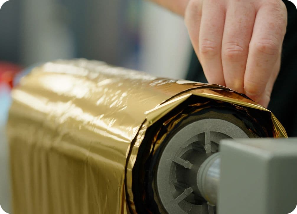 A hand pulling gold foil from a roll, with the foil partially wrapped around a cylindrical core.
