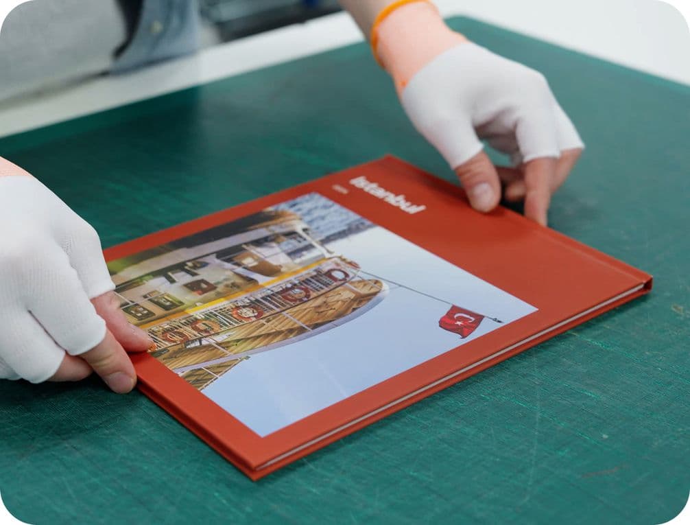 Person with white gloves handling a red book titled "Istanbul" on a green table.