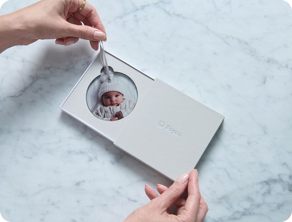 Hands holding a white photo album with a baby picture on the cover, placed on a marble surface.