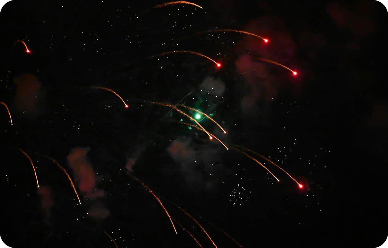 Fireworks with red and green trails against a dark night sky, creating a vibrant, celebratory atmosphere.