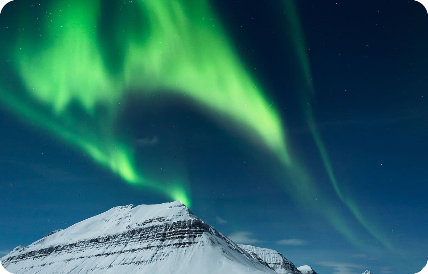 Vivid green aurora borealis dancing over a snow-covered mountain peak under a starry night sky.