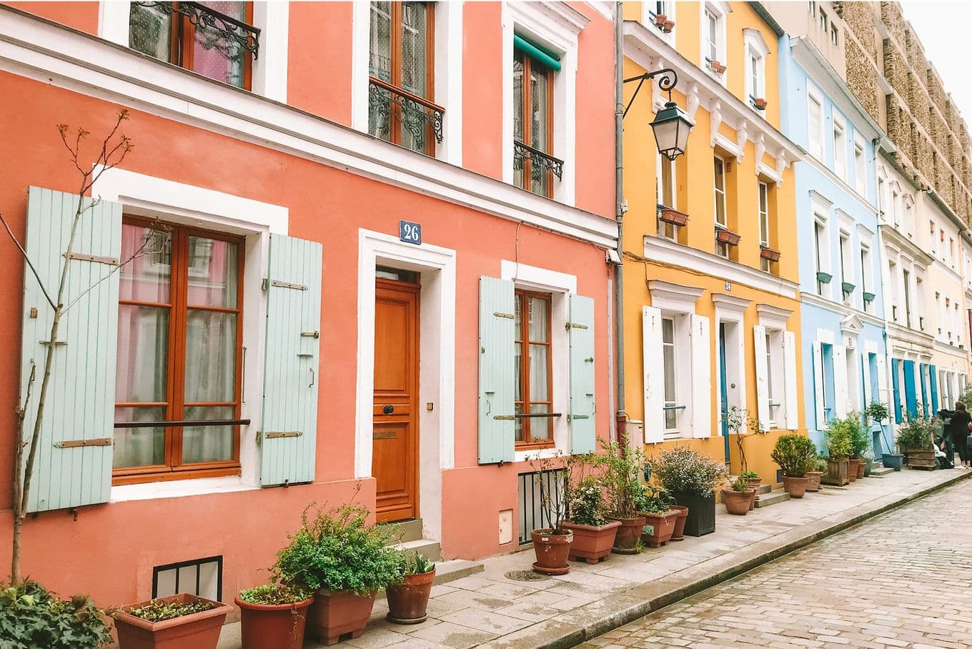 Colorful row of houses with wooden shutters and potted plants lining a cobblestone street under a clear sky.