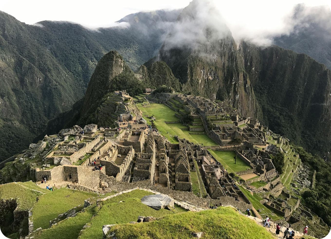 Aerial view of Machu Picchu, an ancient Incan city with stone structures and terraces, surrounded by lush green mountains and misty clouds.