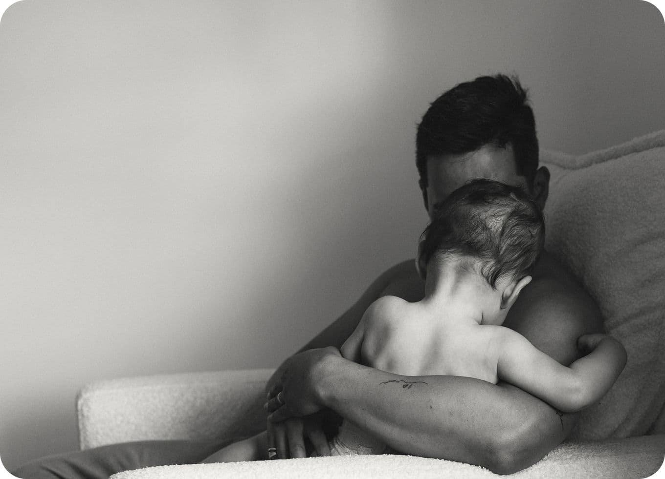 A person lovingly embraces a small child on a couch in a softly lit room, creating an intimate and tender moment.