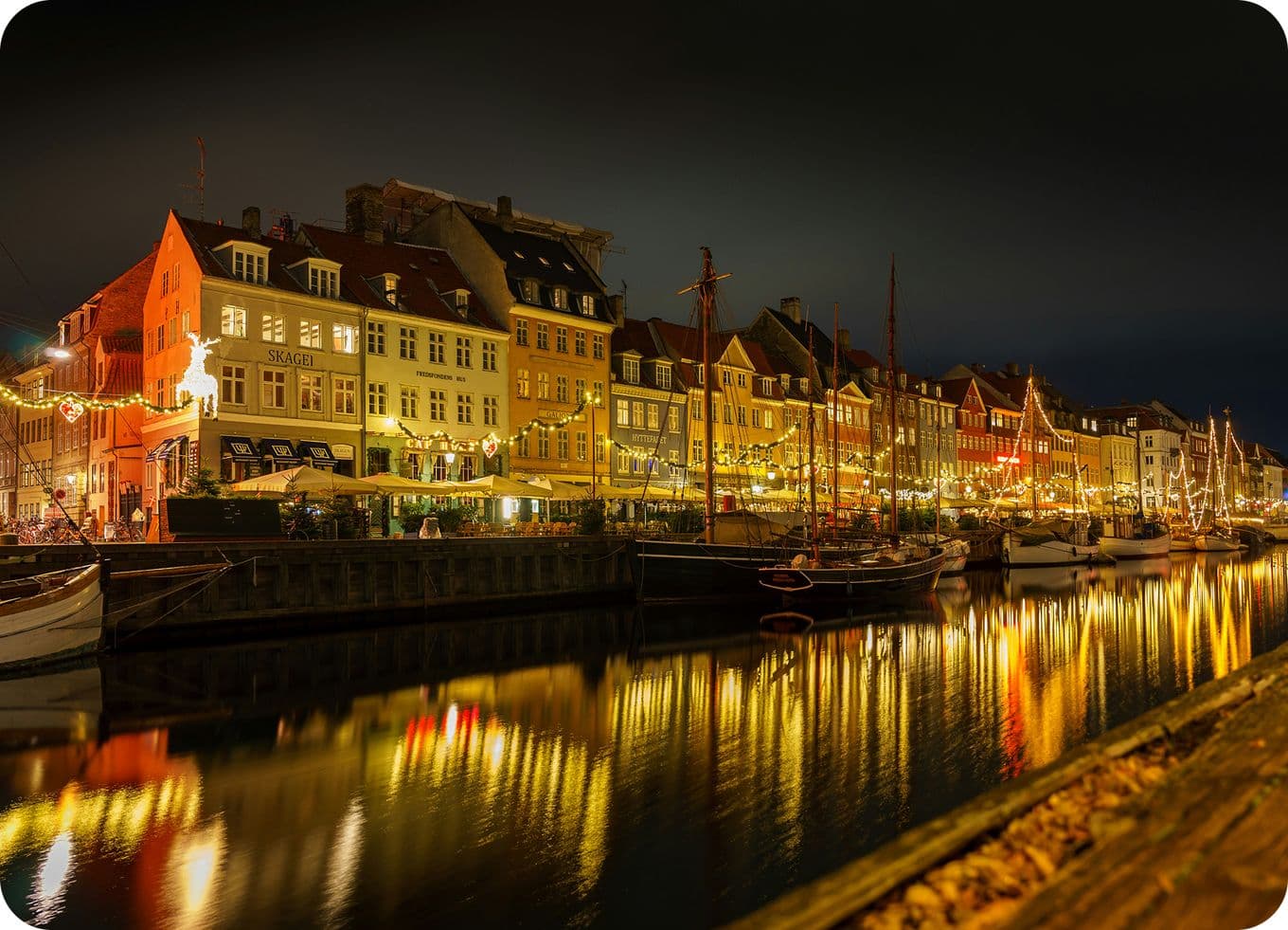 Night view of a canal lined with illuminated, colorful buildings and boats reflecting on the water, creating a warm and inviting atmosphere.