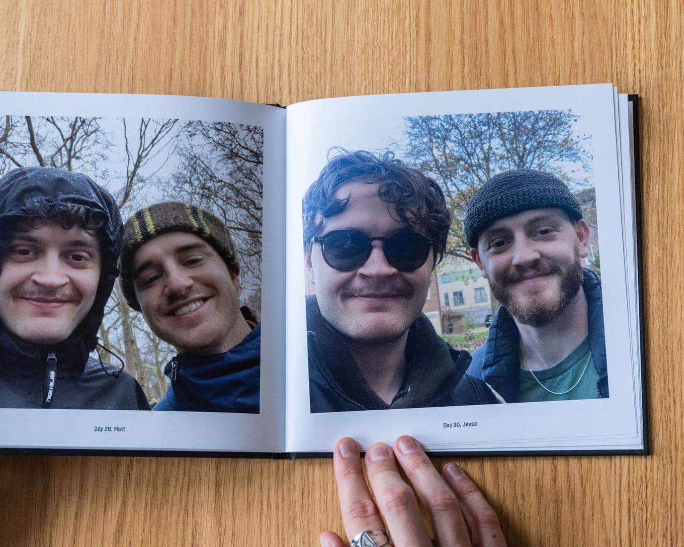 Open photo book showing two pages of three friends posing outdoors, smiling. One wears sunglasses; bare trees are in the background.