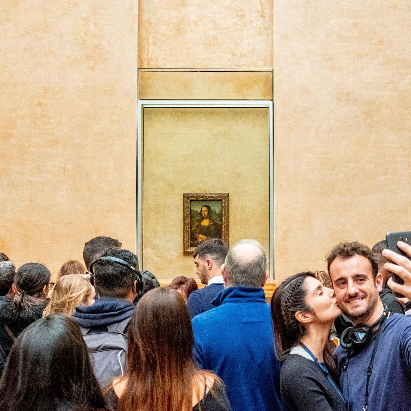 A couple taking a selfie among crowds of people viewing the Mona Lisa painting inside the Louvre, Paris, France