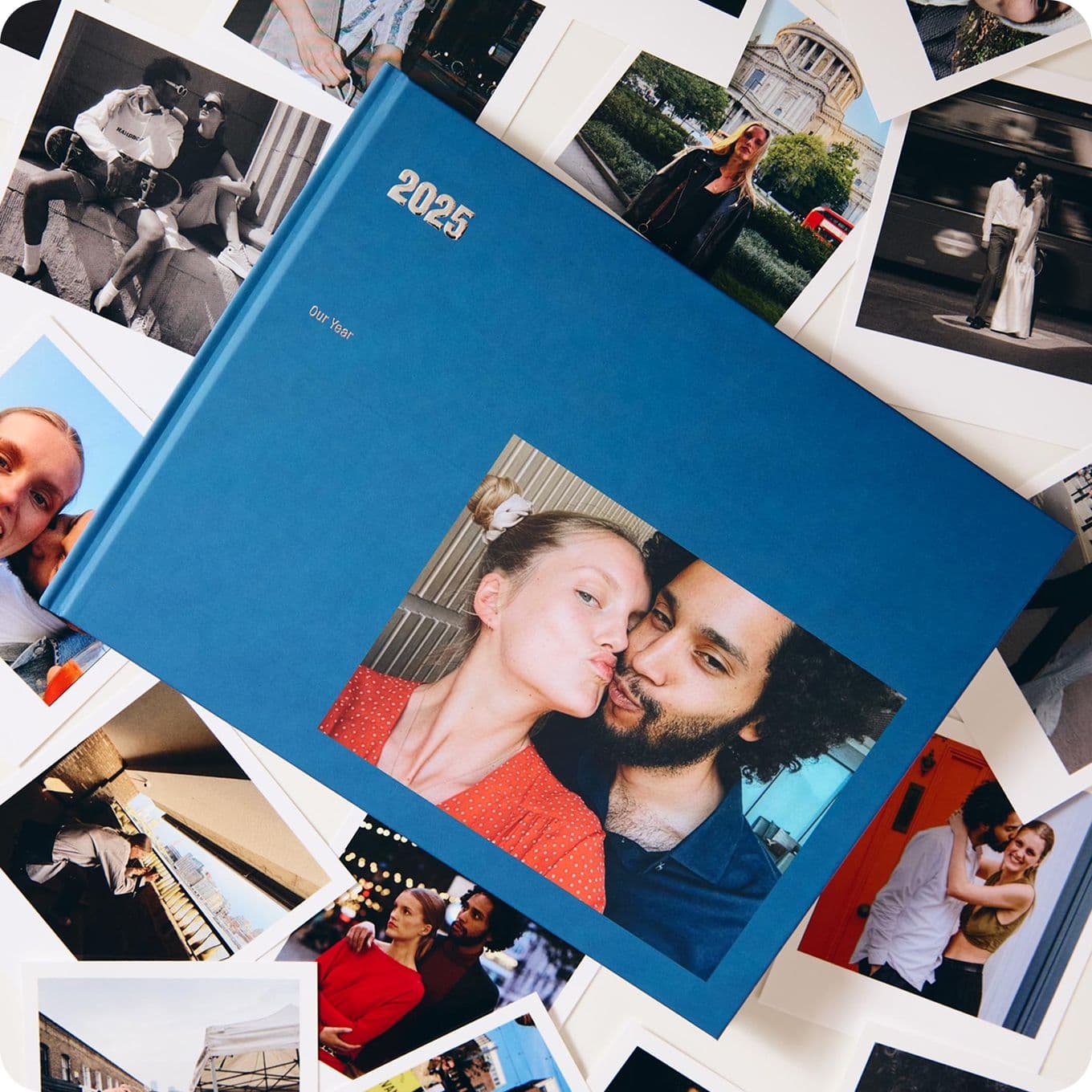 A blue photo album labeled "2025" surrounded by various candid photos. The cover features a couple taking a selfie.