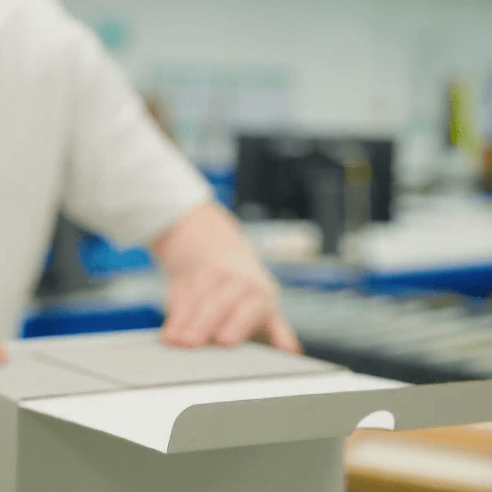 Person in a white shirt assembling a cardboard box in a blurred industrial setting.