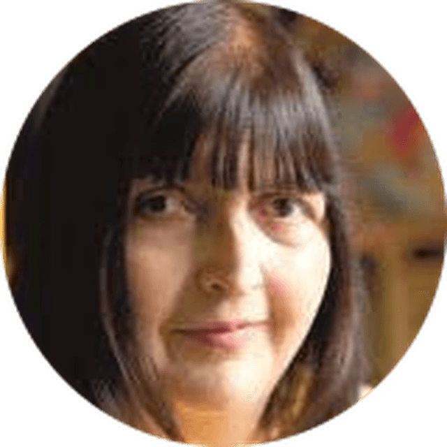 A woman with straight, dark hair and bangs, looking at the camera with a neutral expression. Blurred background.