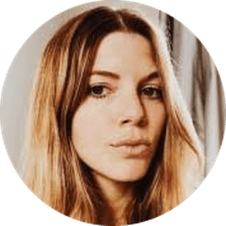 A woman with long, light brown hair and a neutral expression looking at the camera. She is indoors with soft lighting.