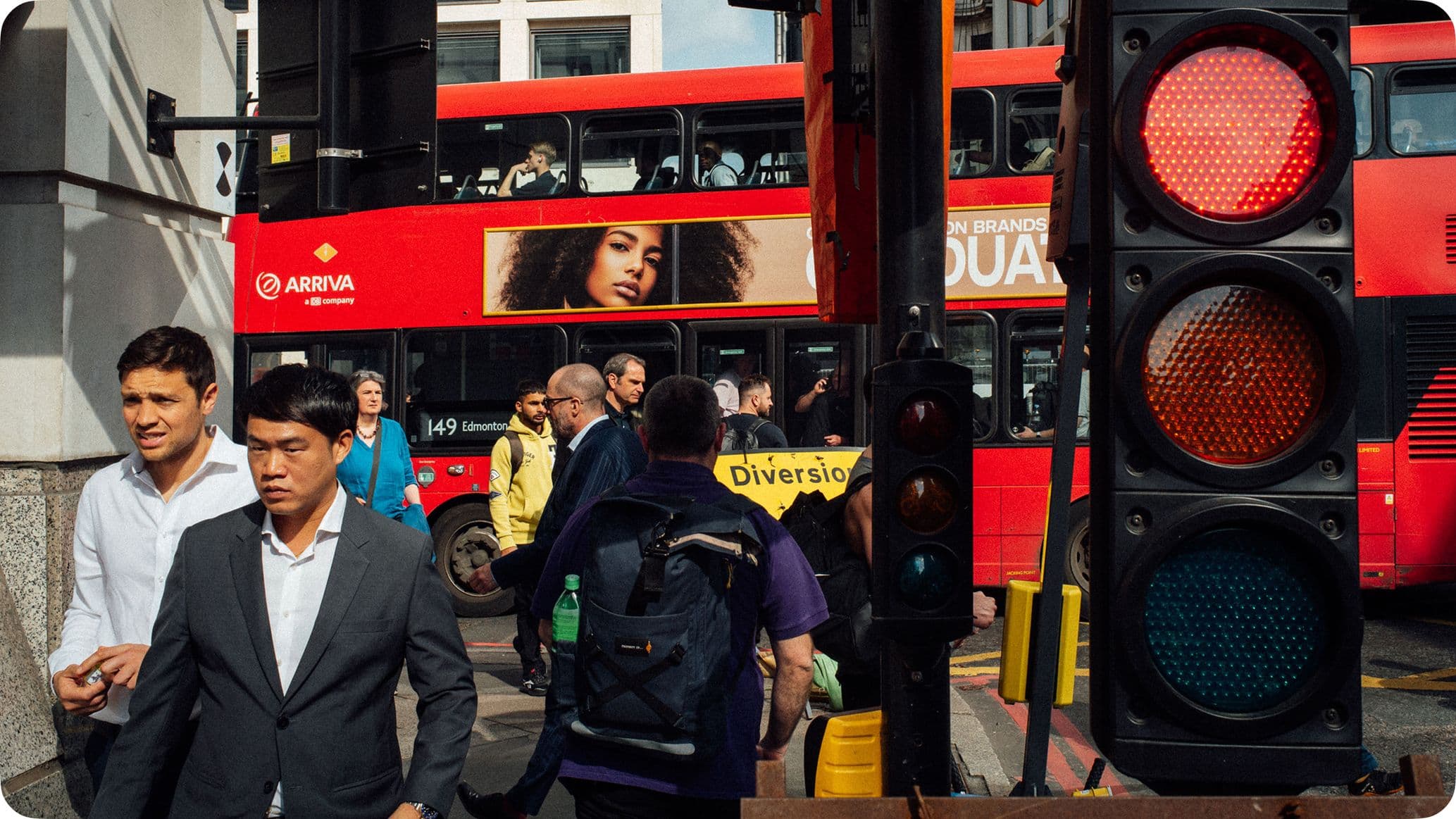 Busy street scene with pedestrians, a red double-decker bus, and a traffic light showing red. A "Diversion" sign is visible.
