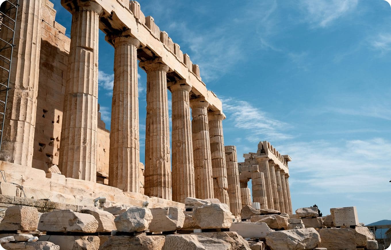 The image shows the Parthenon in Athens, Greece, with its iconic columns under a clear blue sky.