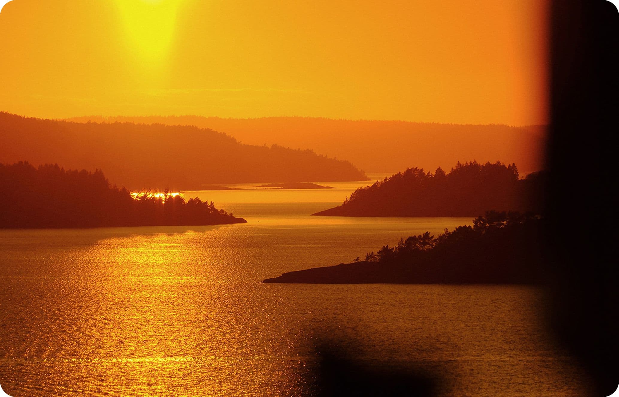 Golden sunset over calm water with silhouetted islands and glistening reflections.