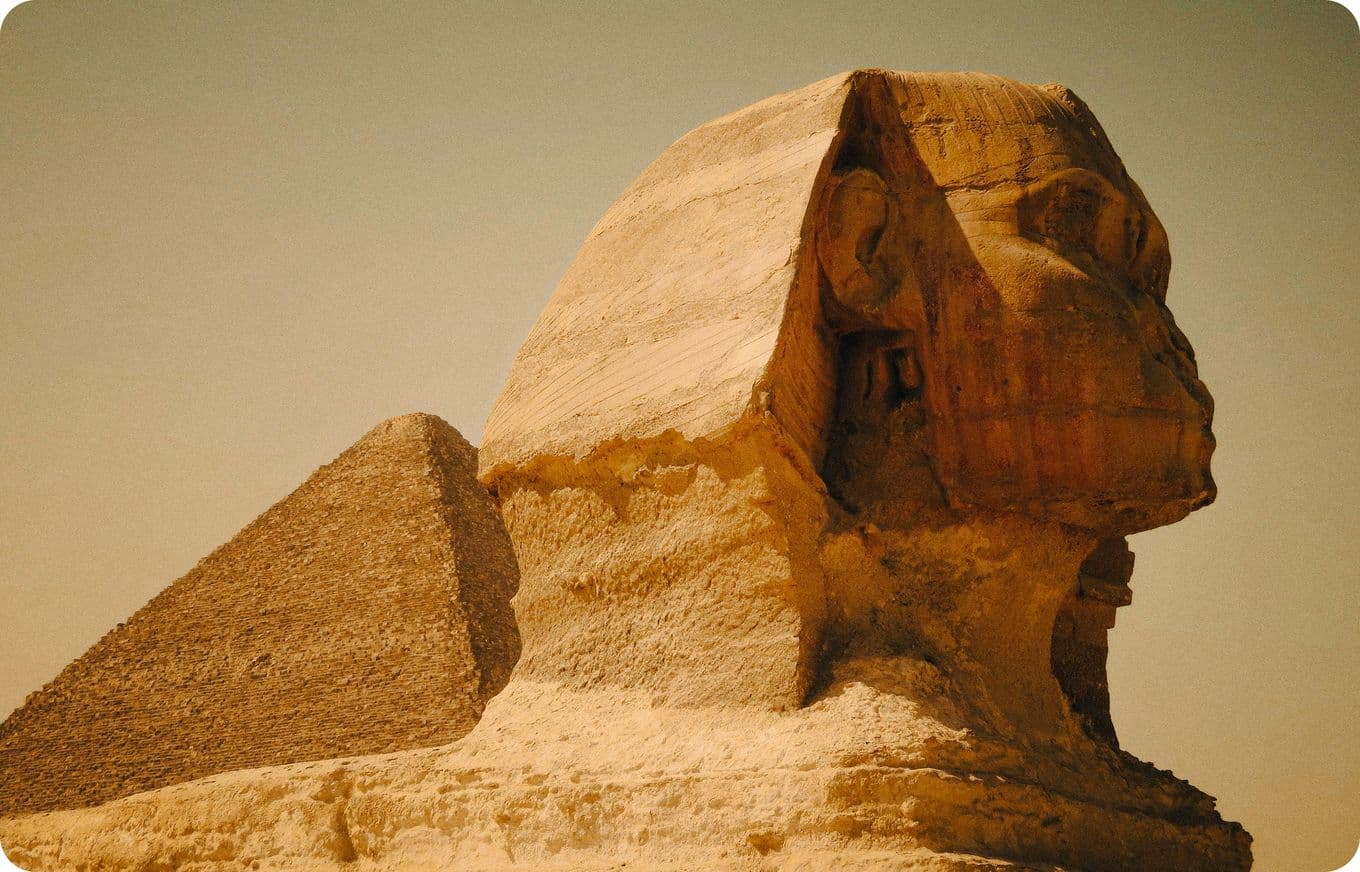 Side view of the Great Sphinx of Giza with the Pyramid of Khafre in the background under a clear sky.