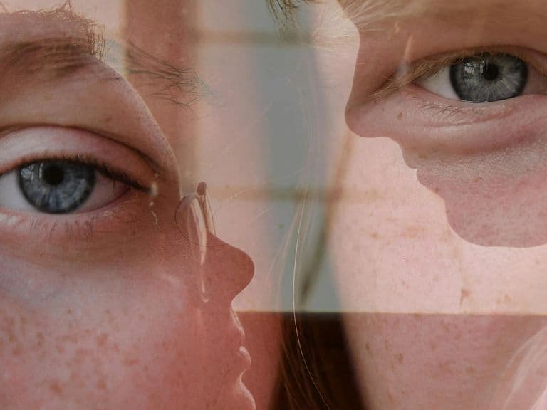 Close-up of a person's blue eyes and face, with a reflective overlay creating a layered effect.