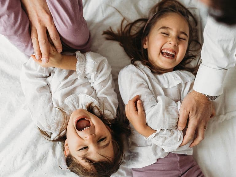 Young sisters giggling and squirming while being tickled by their parents on a bed