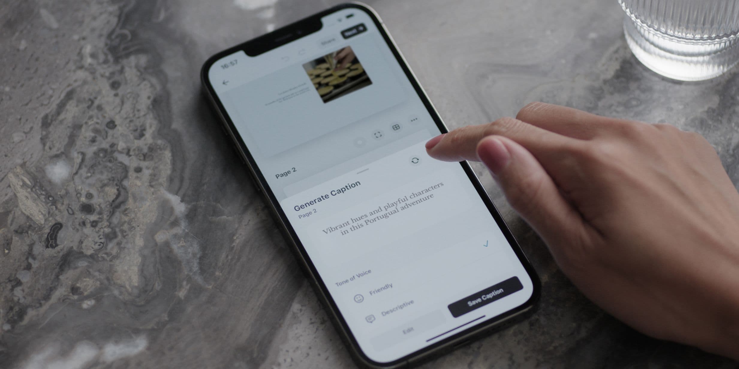 Hand interacting with a smartphone on a marble surface, displaying a caption generation app. A glass of water is nearby.