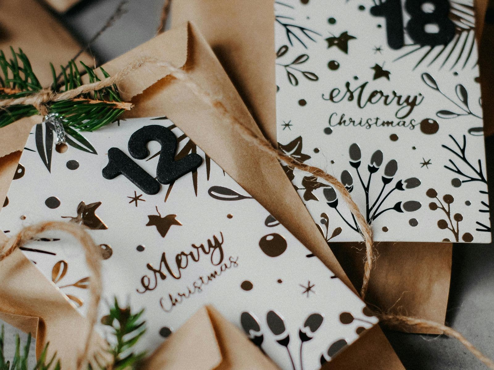 Festive envelopes with "Merry Christmas" cards, adorned with pine sprigs and twine, featuring numbers 12 and 18.