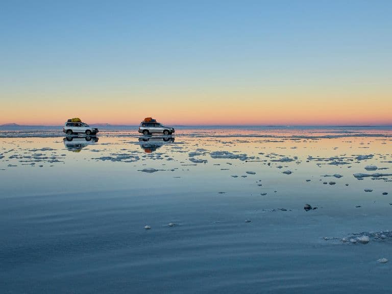 Two touring cars drive across salt flats, Uyuni, Bolivia