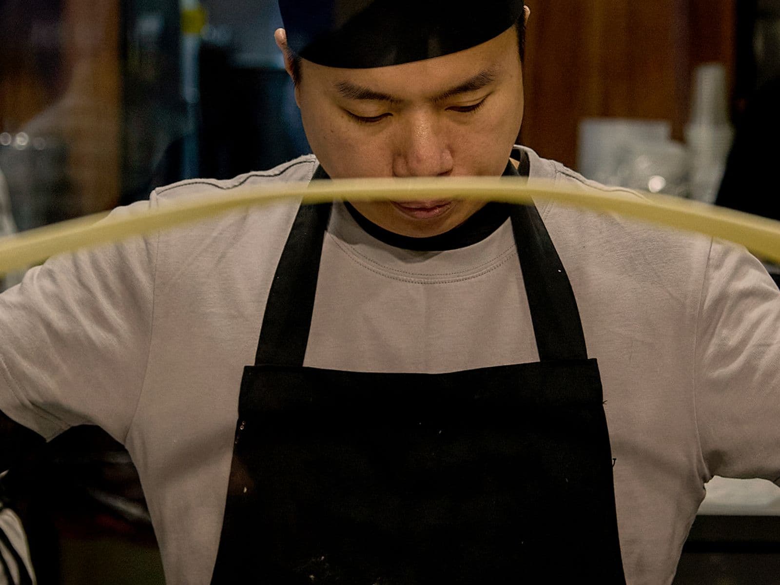 A chef in a black apron and hat stretches dough.