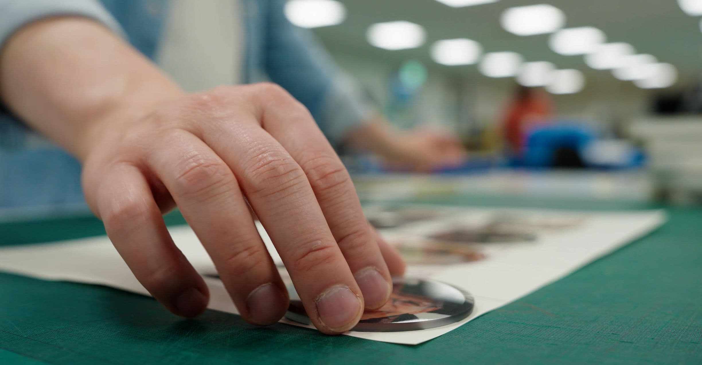 A hand placing a circular photo on a sheet, with a blurred background of a room with bright lights.