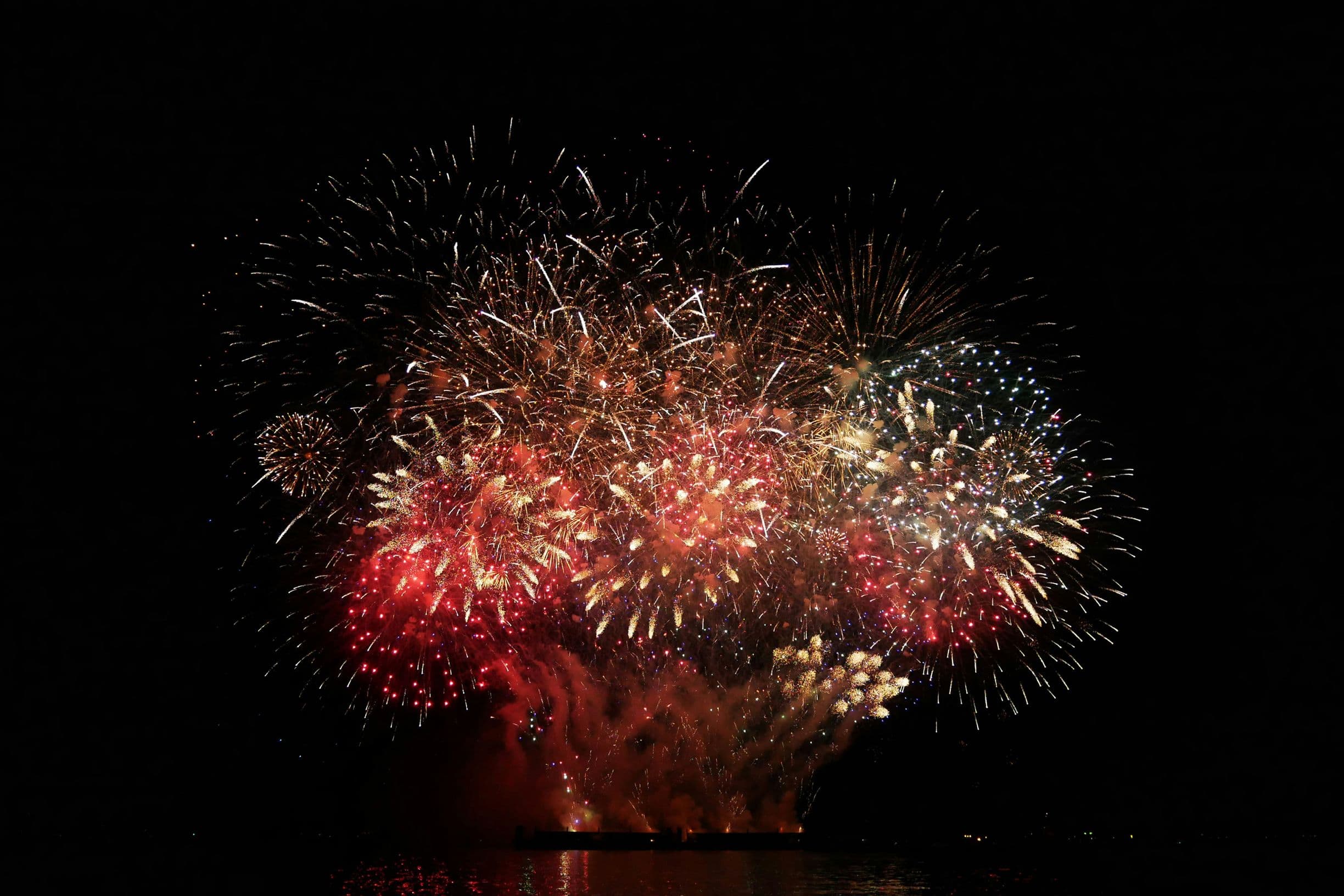 Colorful fireworks burst against a dark night sky, reflecting over water.