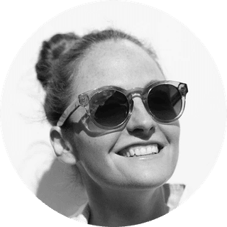 Smiling person wearing sunglasses, hair in a bun, and looking upward against a white background. Black and white photo.