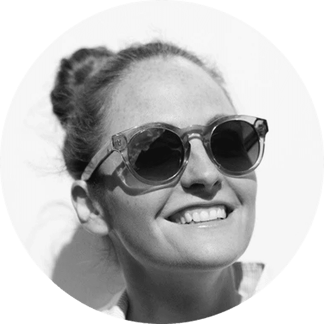 Smiling person wearing sunglasses, hair in a bun, and looking upward against a white background. Black and white photo.