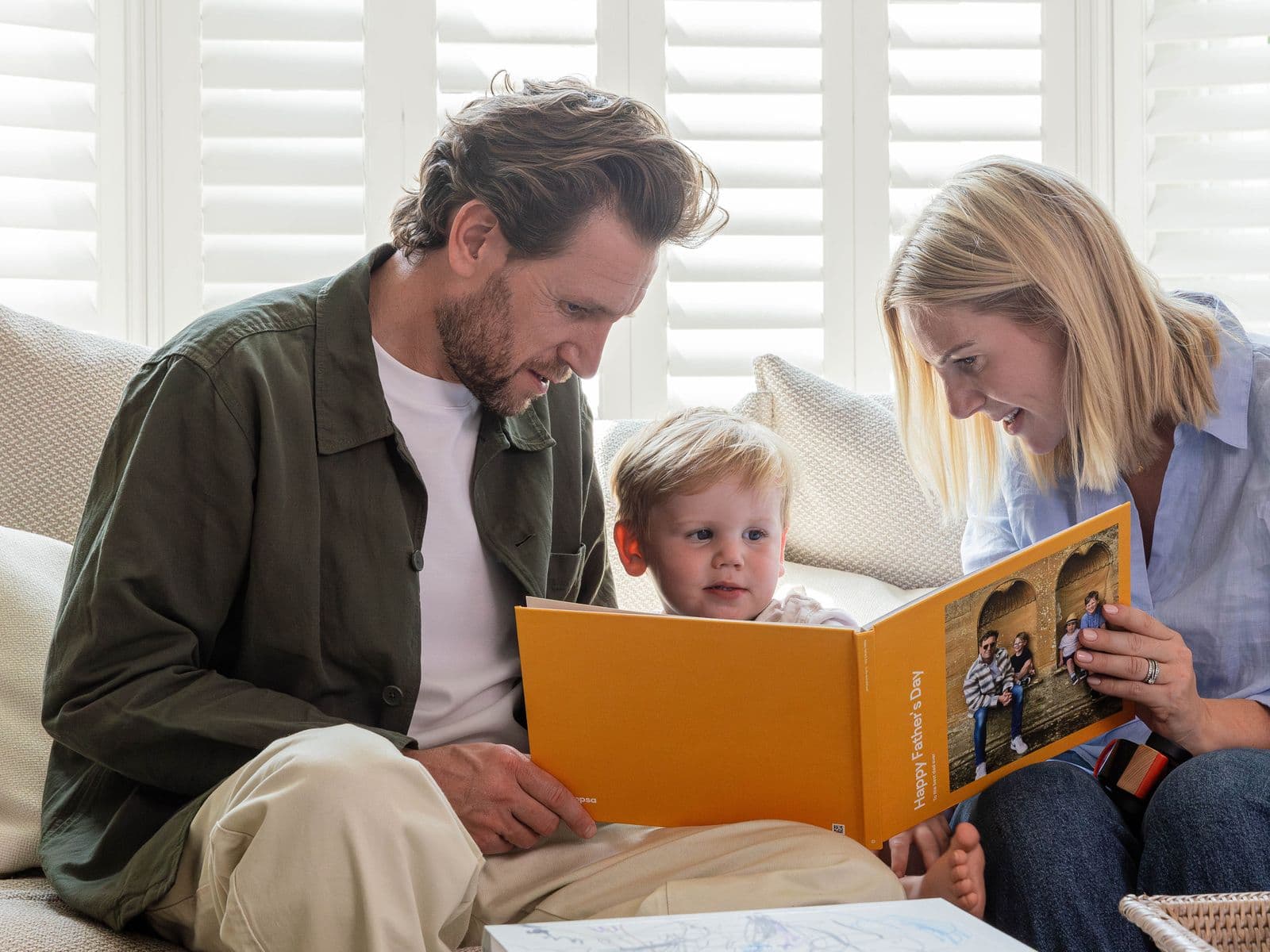 A mother and young child present the child's father with a Father's Day-themed Photo Book
